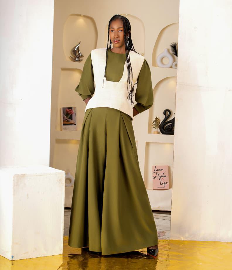 Sakina en robe verte à manches bouffantes, gilet écru structuré, décor alcôves, sol jaune, lumière douce